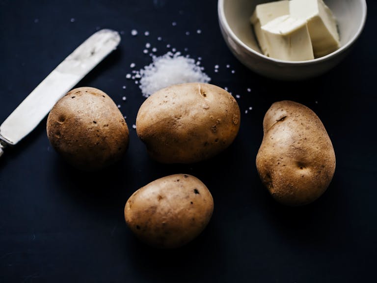Artistic still life showcasing potatoes, butter, and salt on a dark background.