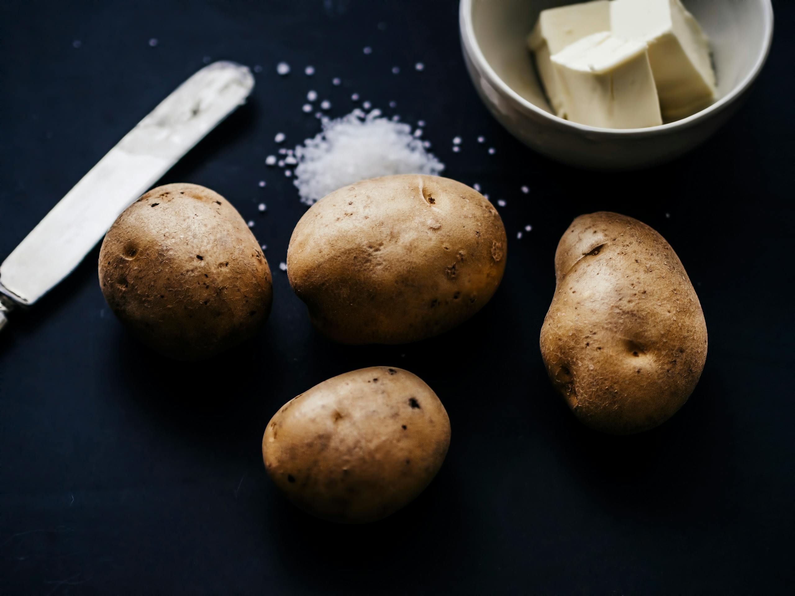 Artistic still life showcasing potatoes, butter, and salt on a dark background.