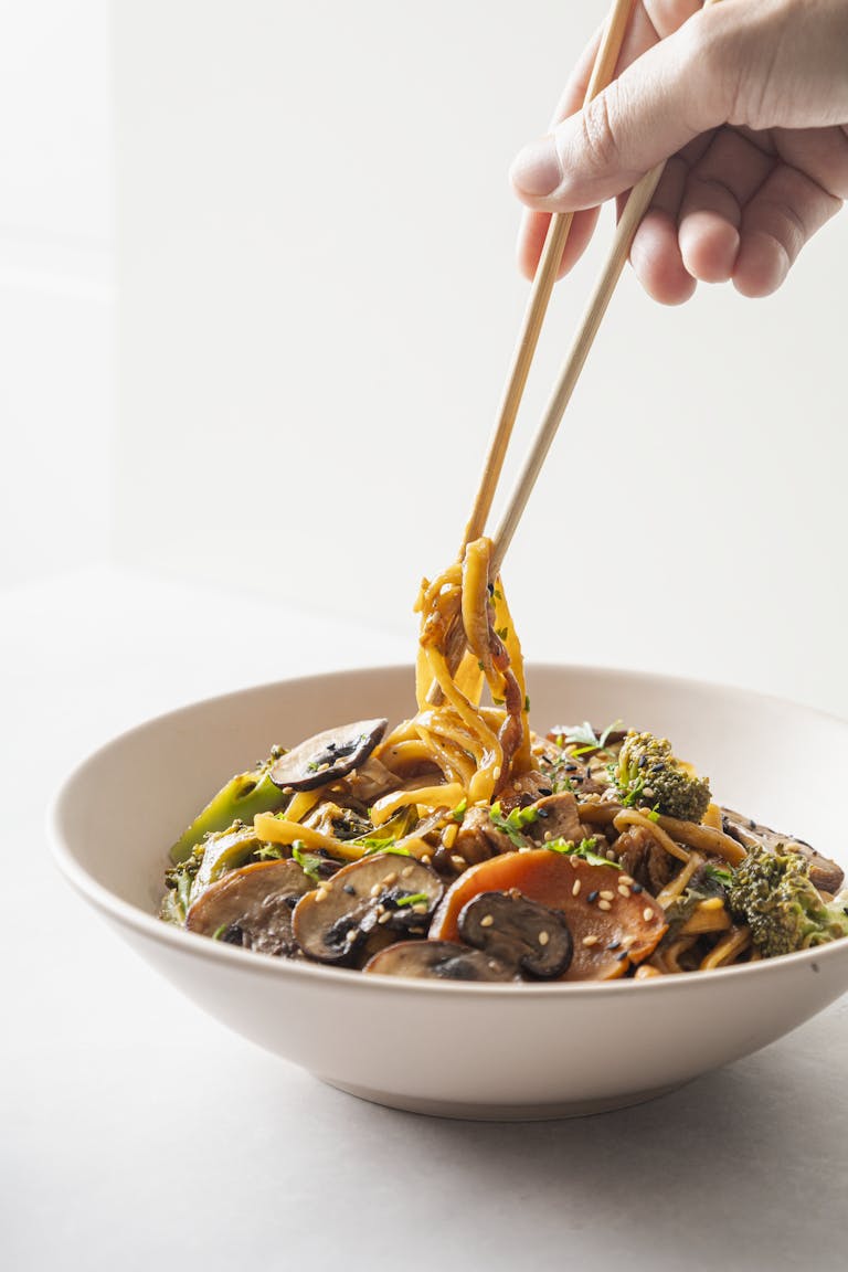 Fresh vegetable noodle bowl being lifted by chopsticks, showcasing healthy dining.
